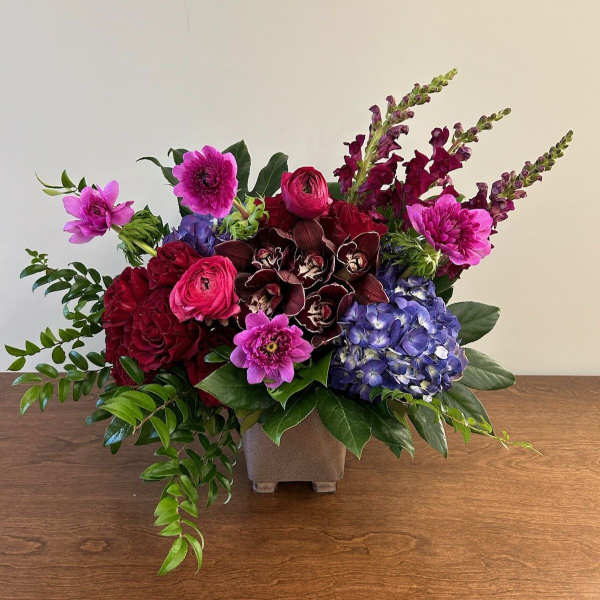 Mixed bouquet in a square vase with pink, red, purple, and blue flowers