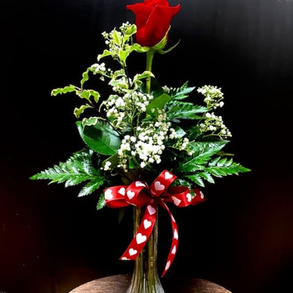 Single red rose in a glass vase with baby's breath and a heart ribbon