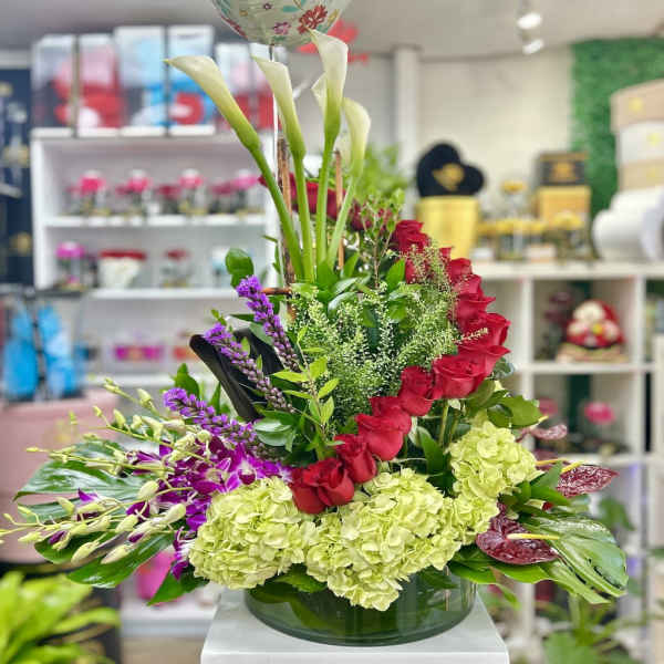 Tall arrangement of white calla lilies, red roses, green hydrangeas and purple orchids in a glass vase