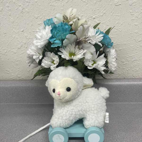 Plush lamb toy on a blue pull cart with white and blue flowers behind it