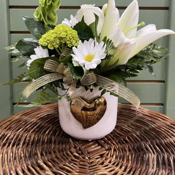 White lilies and daisies in a white vase with a gold heart ornament