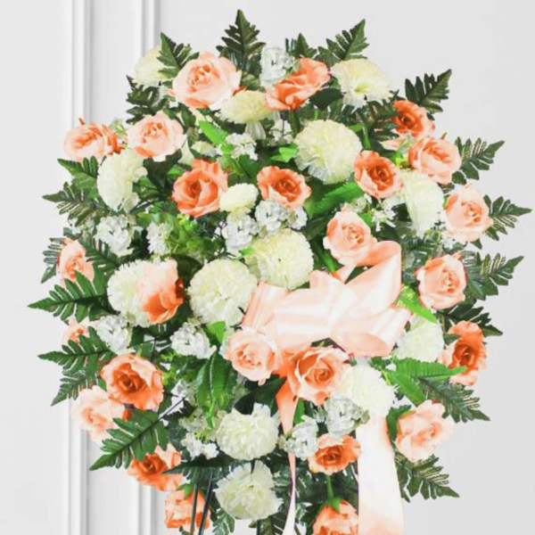 Peach roses and white carnations arranged in a standing wreath with a ribbon