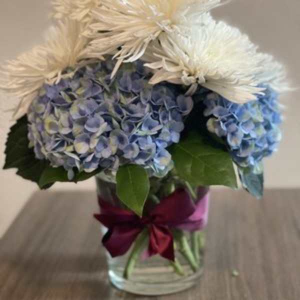 Blue hydrangeas and white spider mums in a glass vase with a ribbon