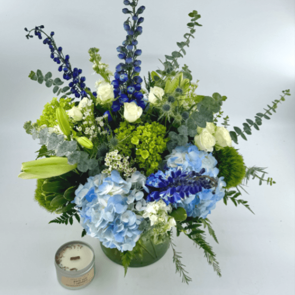 Blue and white floral arrangement in a green vase with a candle beside it