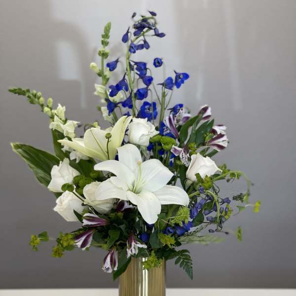 White lilies and blue flowers arranged in a gold vase