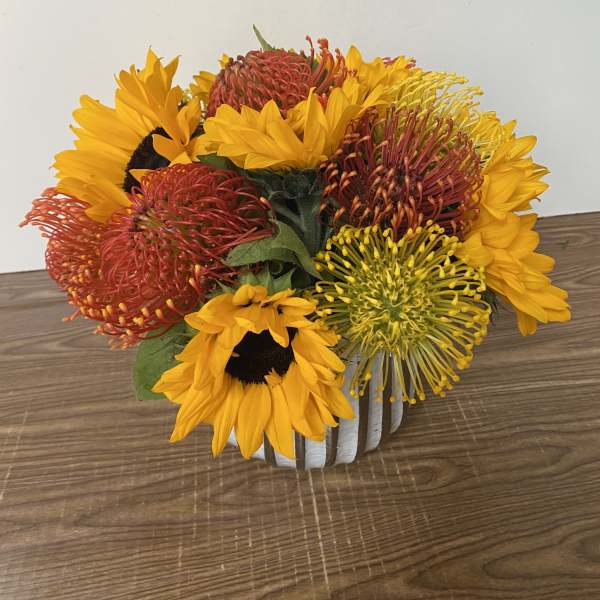 Bouquet of sunflowers and red pincushion protea in a white container