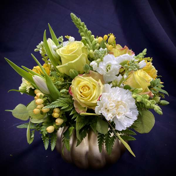 Yellow roses and white flowers arranged in a bronze pumpkin vase