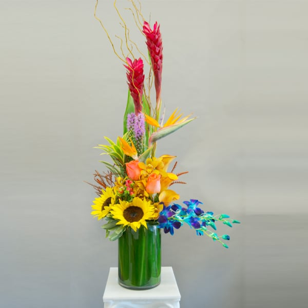 Tall tropical bouquet with sunflowers and orchids in a glass vase