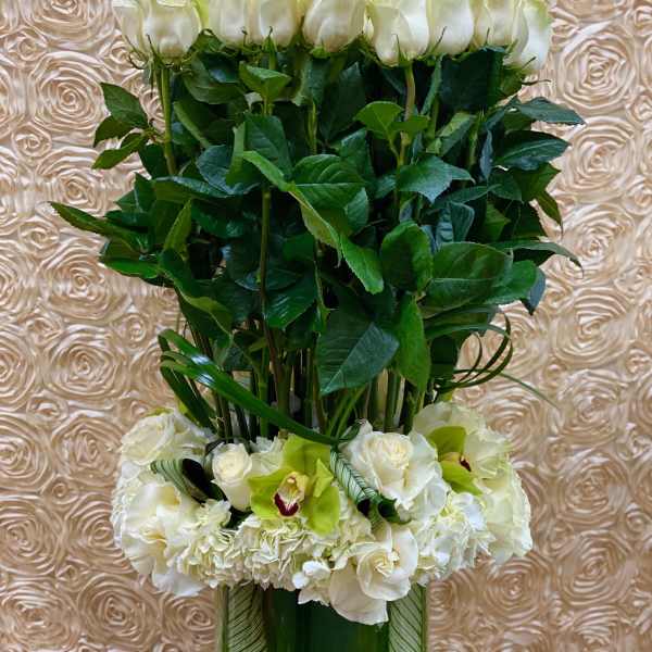 Tall white rose arrangement with orchids and hydrangeas in a glass vase