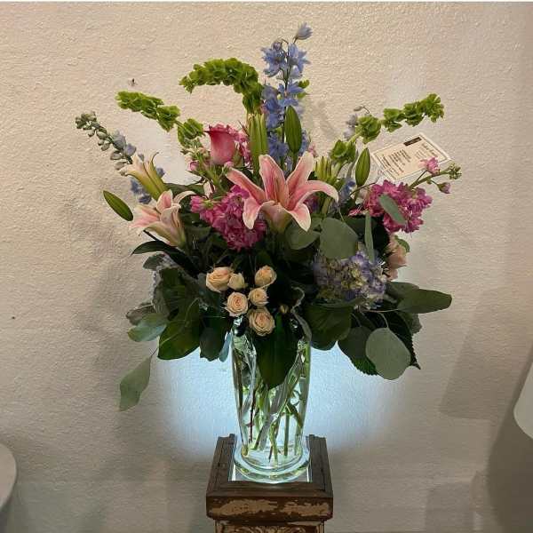 Tall mixed bouquet with pink lilies, roses, and blue flowers in a glass vase