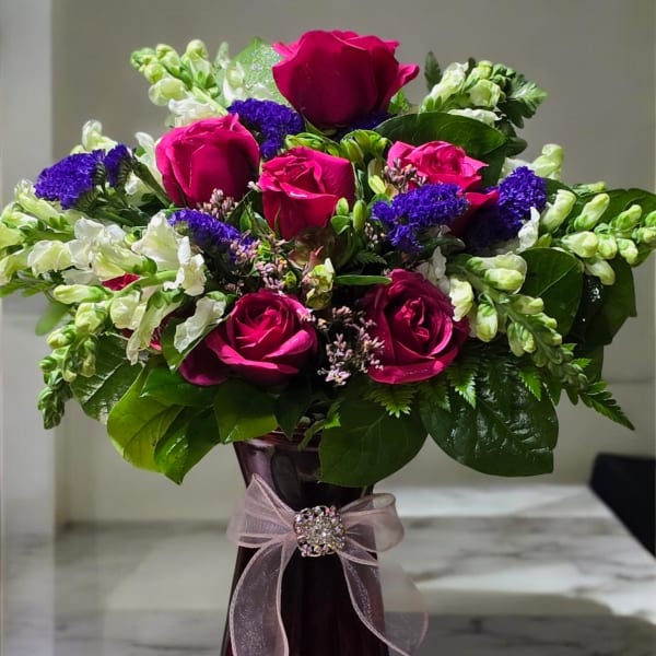 Bouquet of pink roses and purple flowers in a tall vase with a ribbon