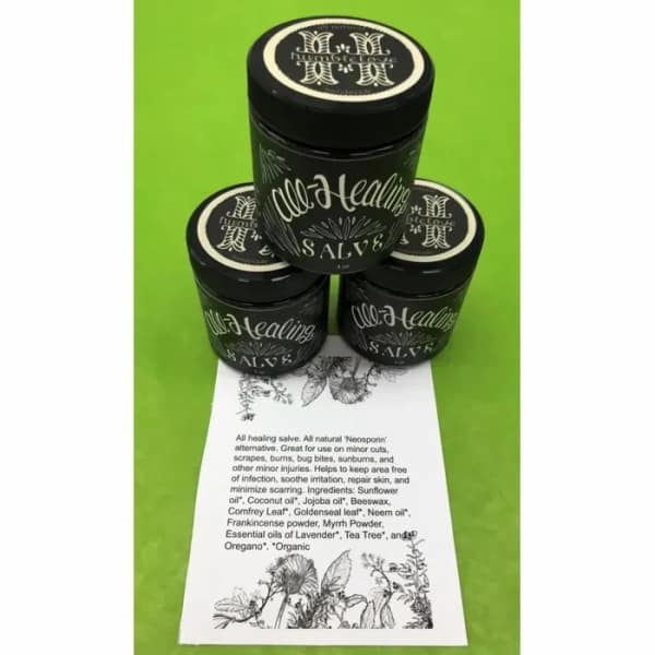 Three black jars of healing salve stacked on a green background with a product card below.