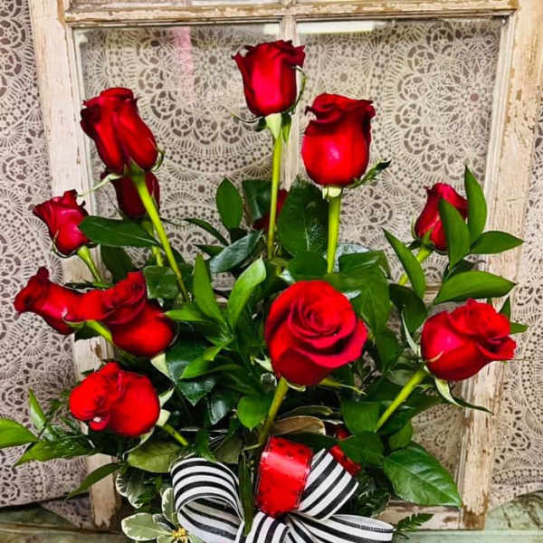 Red roses arranged in a glass vase with a striped ribbon bow