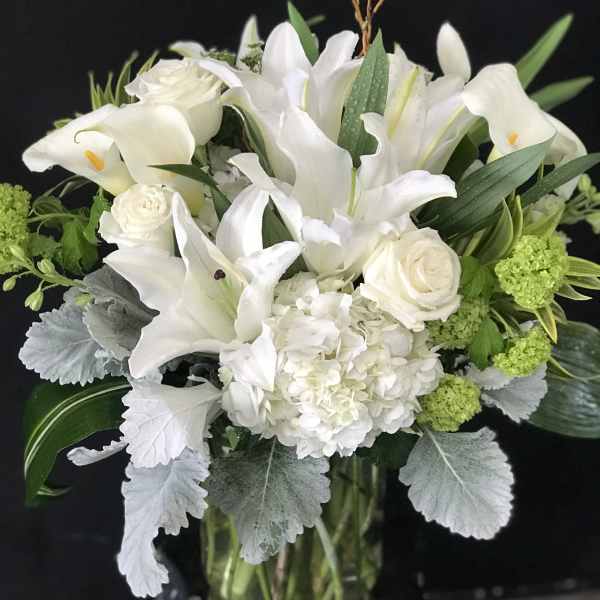 White lilies and roses arranged in a glass vase with green accents