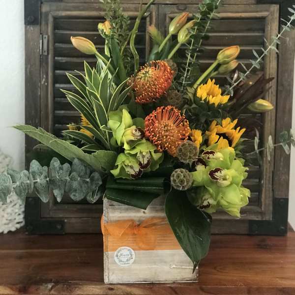 Tropical floral arrangement in a wooden box with orange and green blooms