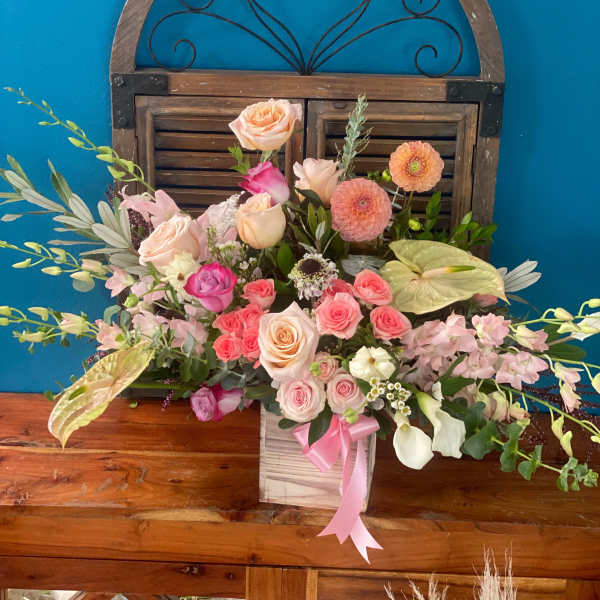 Mixed pink and peach floral arrangement in a wooden box with a pink ribbon