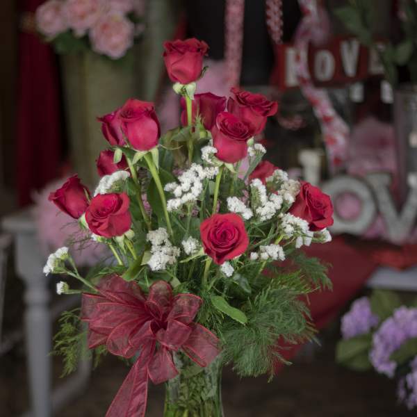 Red roses arranged in a clear glass vase with a red ribbon