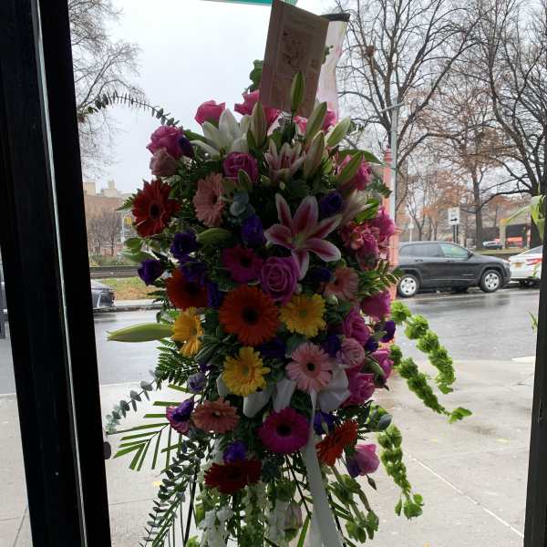 Tall standing spray of mixed pink, white, purple, and yellow flowers with ribbon