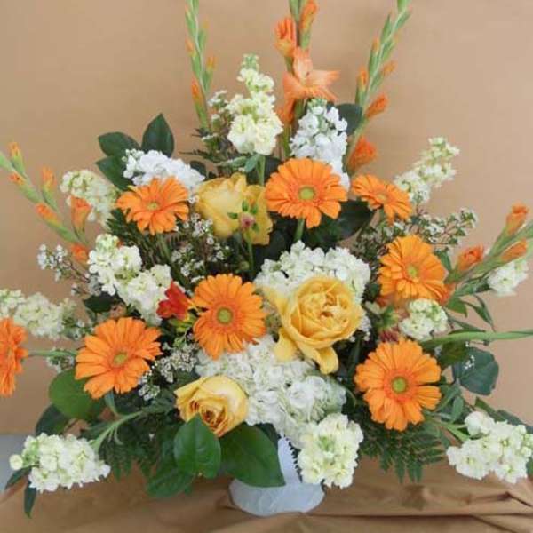 Orange gerbera daisies and yellow roses in a white vase
