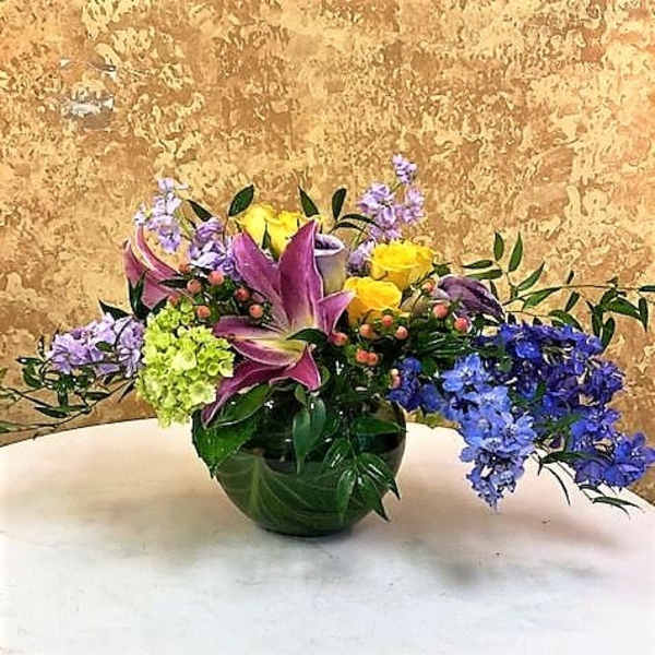 Mixed bouquet of lilies, roses, and blue flowers in a glass vase