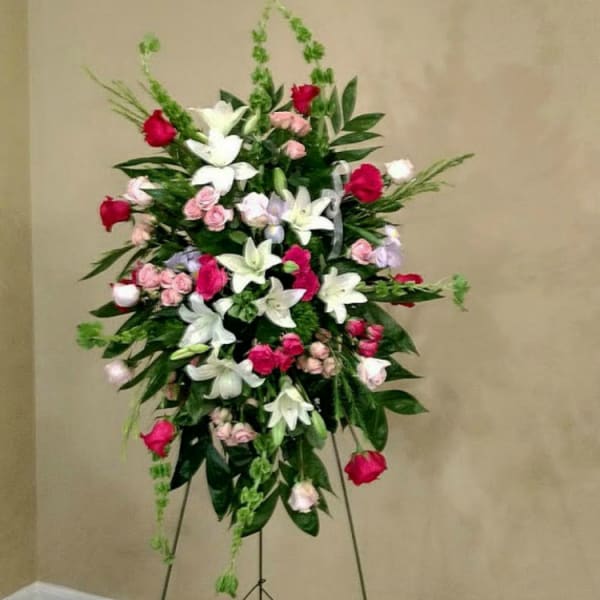Standing floral spray with white lilies, pink roses, and red blooms on an easel