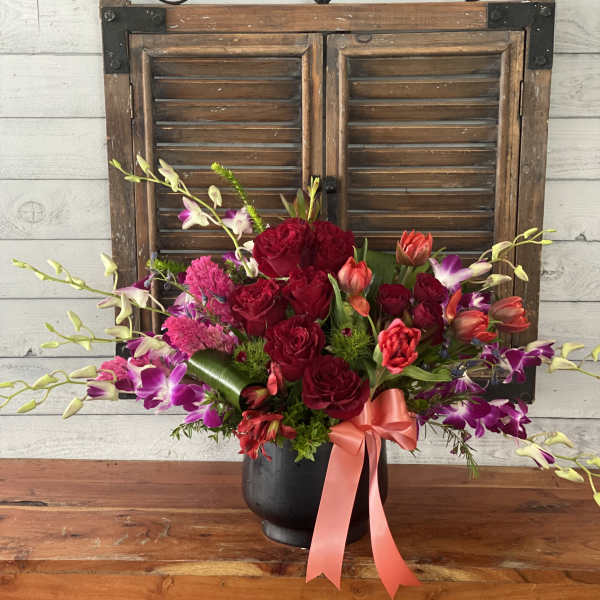 Bouquet of red roses and purple orchids in a black vase with a pink ribbon
