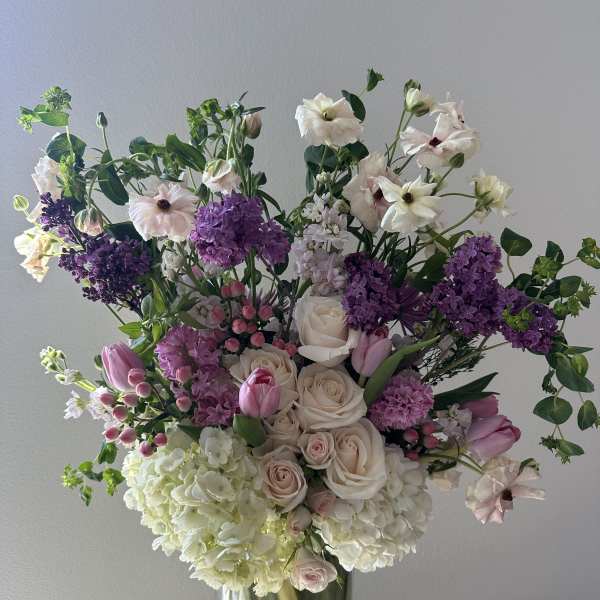 Large bouquet of pale roses, purple blooms, and white flowers in a glass vase