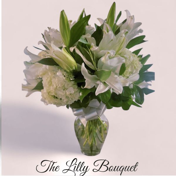White lilies and hydrangeas in a glass vase with a silver ribbon
