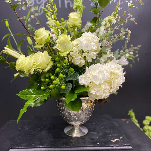 Green and white floral arrangement in a silver urn vase