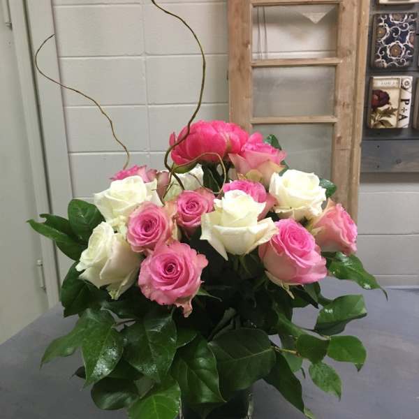 Pink and white roses arranged in a glass vase with curly branches