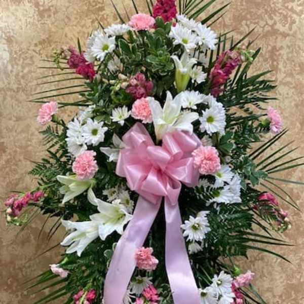 Standing floral spray with white lilies, daisies, and pink carnations, tied with a pink bow