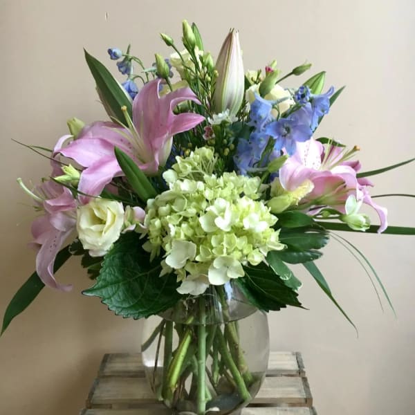 Pink lilies and blue flowers in a clear glass vase