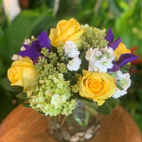 Yellow roses and purple flowers in a glass vase