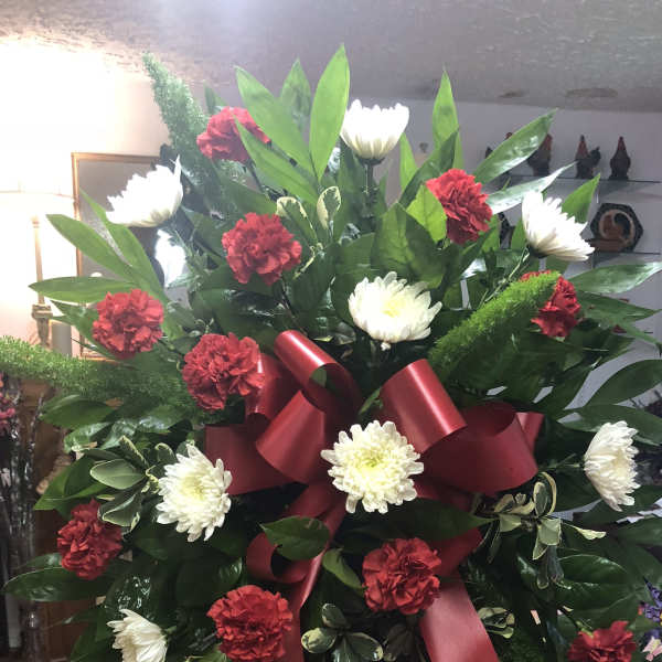 Large standing spray with red carnations and white chrysanthemums tied with a burgundy ribbon