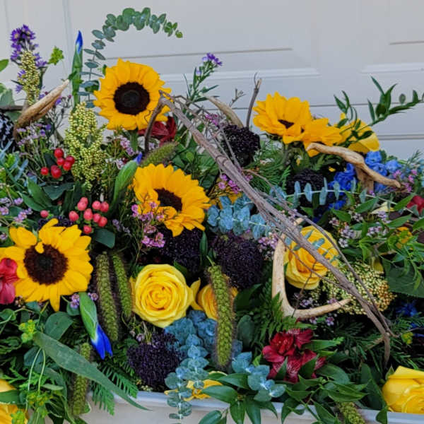 Large floral arrangement with sunflowers, yellow roses, and blue flowers