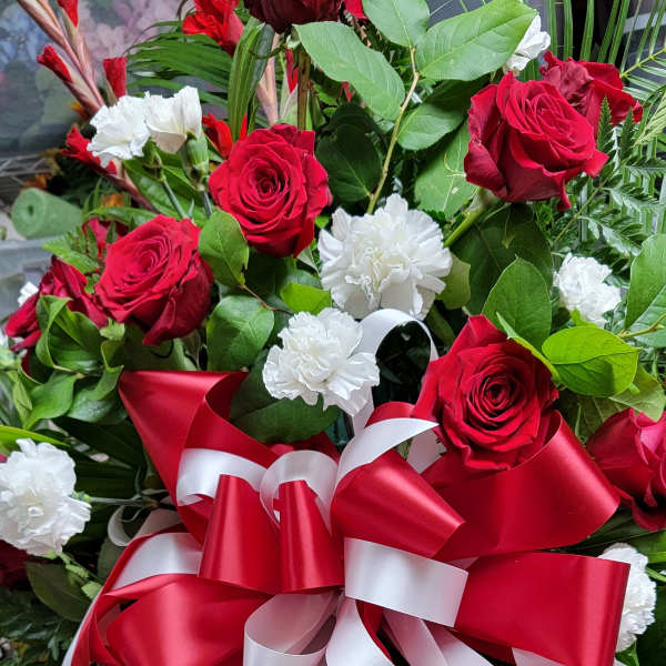 Standing floral spray with red roses, white carnations, and a red-and-white ribbon bow