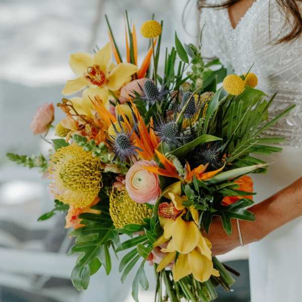 Bride holding a colorful tropical bouquet with yellow orchids and orange blooms