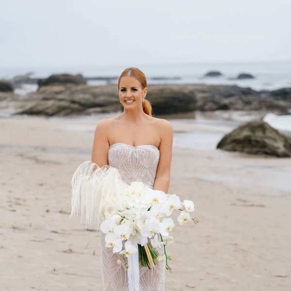 Bride holding a white orchid bouquet on a beach