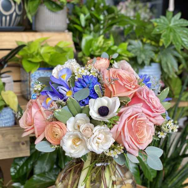 Mixed bouquet of pink roses, white anemones, and blue flowers in a glass vase