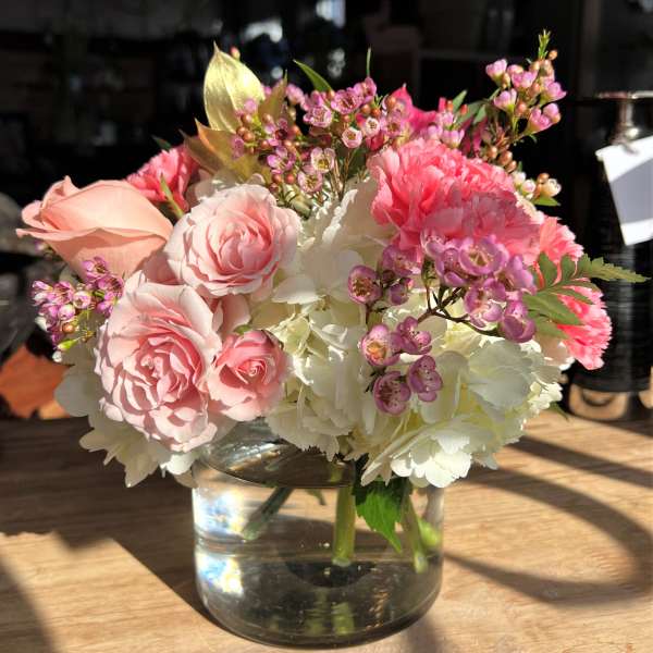 Small arrangement of pink roses and carnations with white hydrangea in a clear glass vase.