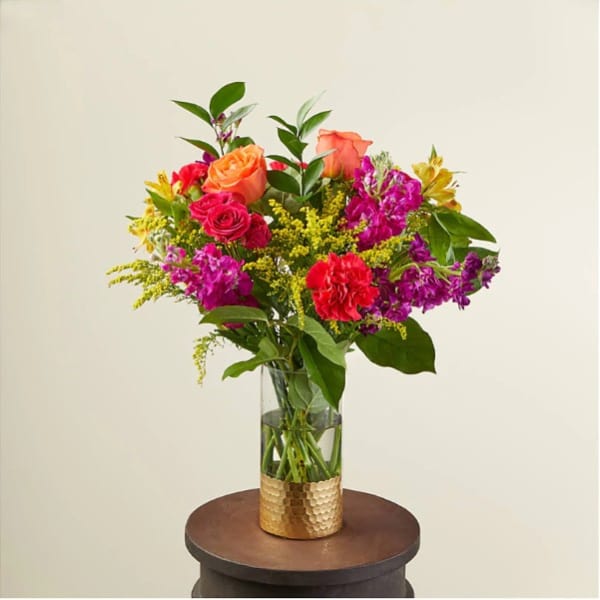 Tall mixed bouquet of bright flowers in a clear vase with a gold base