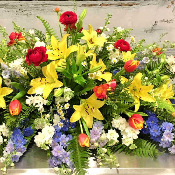 Large mixed floral spray with yellow lilies, red roses, and colorful tulips