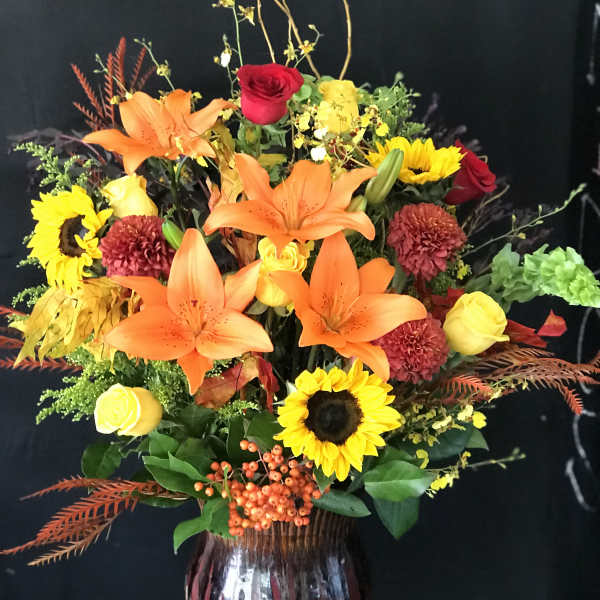 Mixed bouquet with orange lilies, sunflowers, and roses in a vase