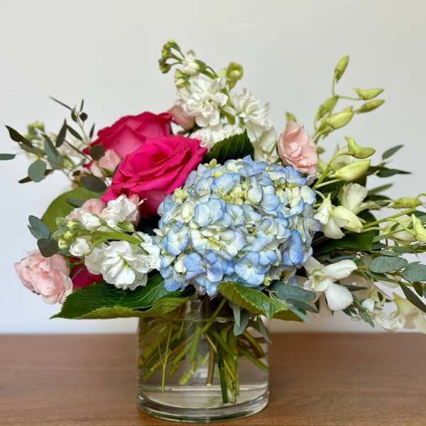 Mixed bouquet with pink roses, blue hydrangea, and white flowers in a glass vase