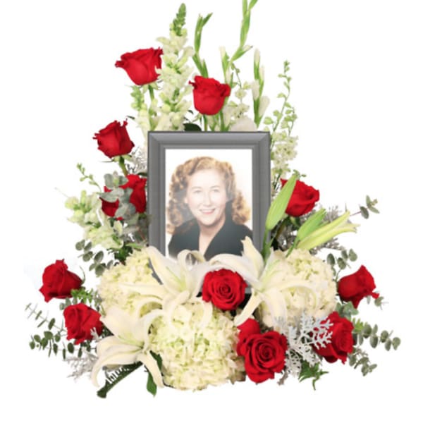 Memorial floral arrangement with red roses, white lilies, and a framed photo