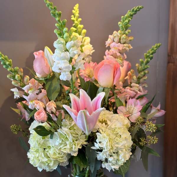 Tall arrangement of pink lilies and roses with white hydrangeas in a clear glass vase