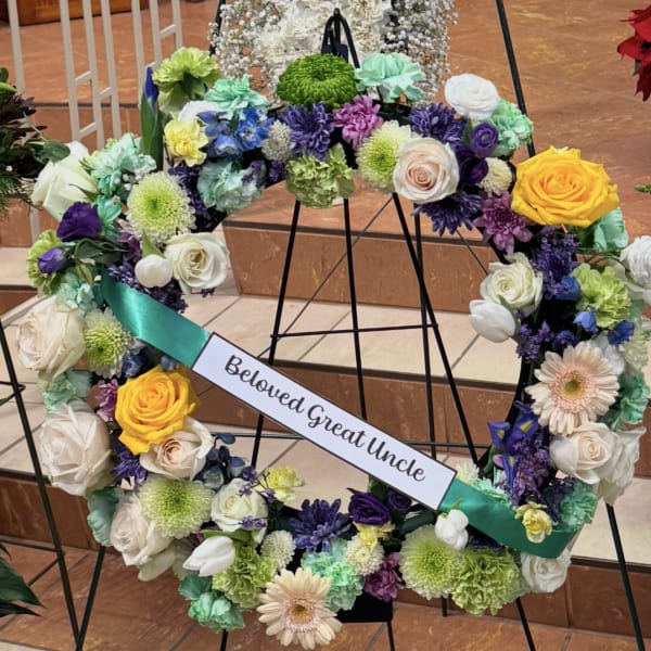 Large floral wreath on an easel with a memorial ribbon reading Beloved Great Uncle
