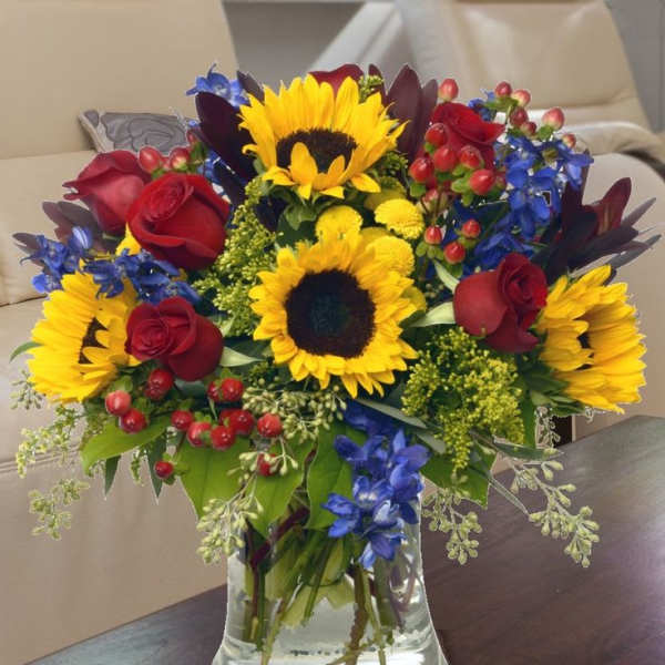 Bouquet of sunflowers, red roses, and blue flowers in a glass vase