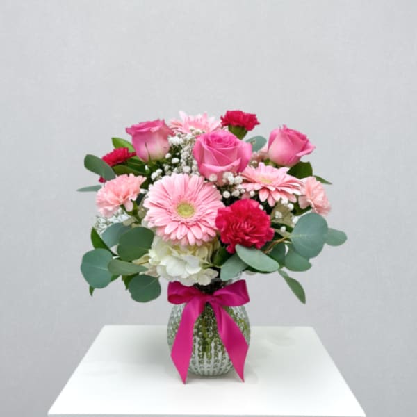 Pink roses, gerbera daisies and carnations in a clear vase with bright ribbon