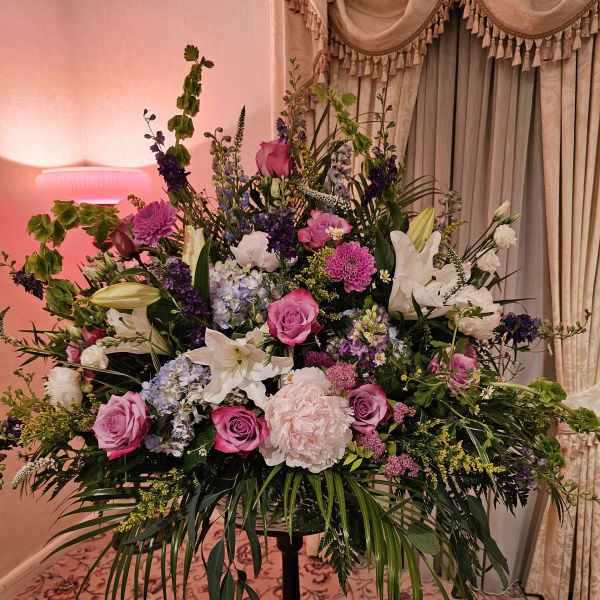 Large mixed floral arrangement on a stand with pink, white, and purple blooms